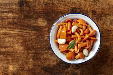 Pickled mushrooms with garlic and a bay leaf, top shot on a dark rustic wooden background with a place for text