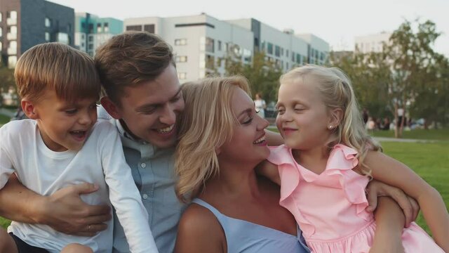 Happy family sit on the grass in the park and laughing close-up. They hugged and talk to each other, smile. Here is a woman and a man and their two small children