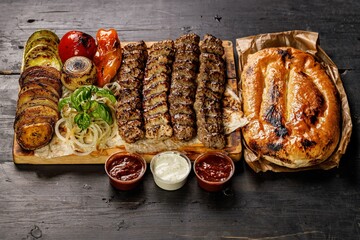 Assorted kebabs from different types of meat. Veal, chicken, lamb kebabs with vegetables and sauces on a wooden board. Traditional Turkish street food. Food delivery service concept. Copy space