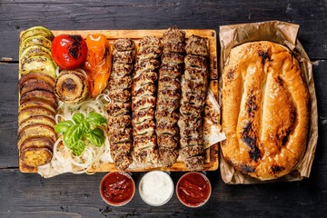 Assorted kebabs from different types of meat. Veal, chicken, lamb kebabs with vegetables and sauces on a wooden board. Traditional Turkish street food. Food delivery service concept. Top view