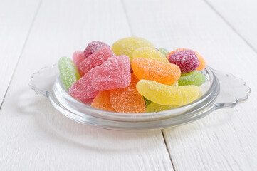 Gummy jelly sugar candies in the form of fruit slices in a bowl on a white wooden background. Holiday concept, baby treats. Unhealthy food.