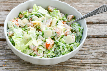 Homemade traditional Caesar Salad with Parmesan Cheese and Croutons in a white bowl on a old white table with leaves and a sauce boat 
