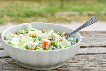 Homemade traditional Caesar Salad with Parmesan Cheese and Croutons in a white bowl on a old white table with leaves and a sauce boat 