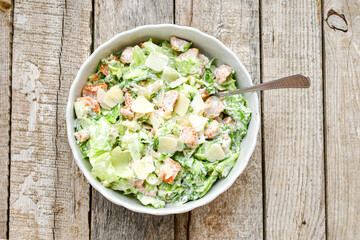 Homemade traditional Caesar Salad with Parmesan Cheese and Croutons in a white bowl on a old white table with leaves and a sauce boat 