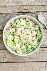 Homemade traditional Caesar Salad with Parmesan Cheese and Croutons in a white bowl on a old white table with leaves and a sauce boat 