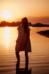 Silhouette of woman in sunset rays. Romantic photo of young beautiful woman standing in water in rays of setting sun and smiling with happiness. 