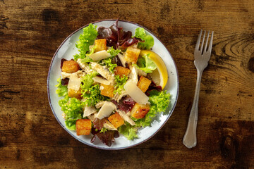 Chicken Caesar salad, shot from the top on a dark rustic wooden background. Romaine leaves, crispy croutons and chicken meat