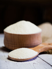 Semolina in a wooden bowl and spoon on a white wooden table, close-up. healthy diet cereals background.