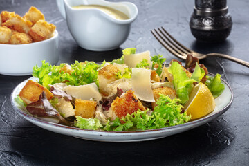 Chicken Caesar salad with the classic mayonnaise based sauce, pepper, and croutons, on a black background