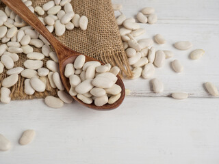 white beans in a wooden spoon on a white wooden table, copy space