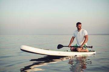 Young man in t-shirt and shorts floating on SUP board
