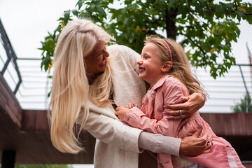 Fototapeta premium A good-looking, modern grandma and granddaughter hug and enjoy together while spending time outdoors on a cloudy, windy day.
