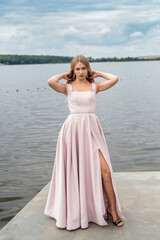 Fototapeta na wymiar Pretty young woman wear in pink fashion evening dress posing near lake in the park