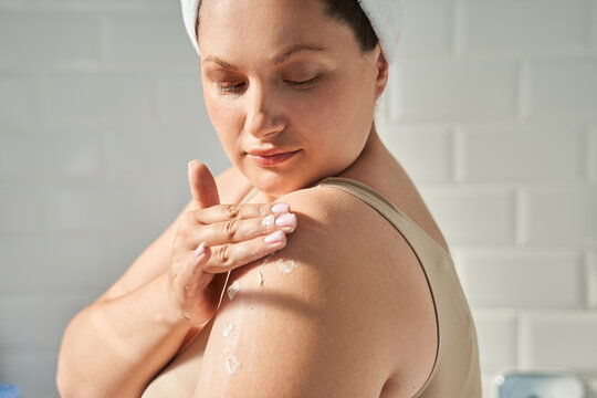 Oversize woman applying cosmetic cream on shoulder