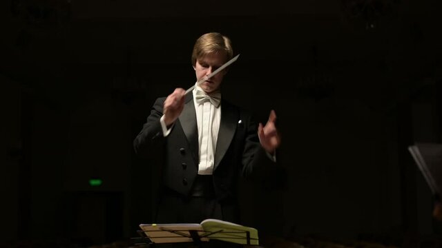 The camera zooms in on the leader of the symphony orchestra. Young conductor leads the orchestra