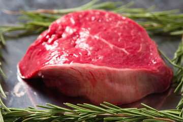One fillet steak on a metal tray and fresh rosemary herb. Butcher craft product. Finest cut of...