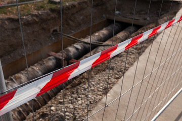 Red and white striped tape restricting access to construction site and pipes in ground