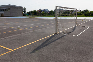 Empty school soccer field playground with goal with net and yellow markings on ground, school building in background