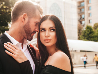 Beautiful fashion woman and her handsome elegant boyfriend in suit. Sexy brunette model in black evening dress. Fashionable couple posing in the street in Europe. Brutal man and his female outdoors