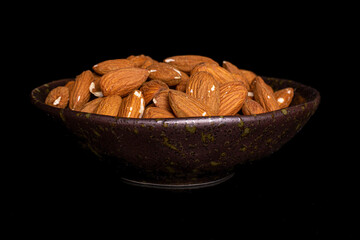 Lot of whole almond in dark ceramic bowl on black glass