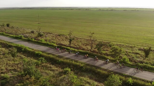 A group of cyclists riding along a road at sunset in the sunlight. Aerial view.