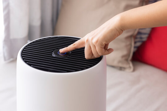 Close-up Asian woman hand, pressing a button on air purifier machine in a bedroom. Protect PM 2.5 dust and air pollution concept. air cleaner removing fine dust in house