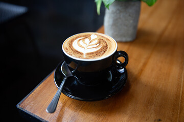 Cup of tasty cappuccino with latte art on wooden table background.