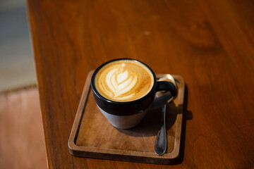 Cup of tasty cappuccino with latte art on wooden table background.