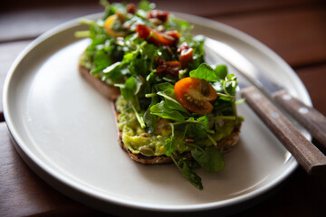 Healthy toast with avocado, arugula and sun dried tomatoes on rustic wooden table.