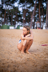 Young white woman in swimsuit sitting with trees behind on sand