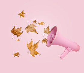 Pink megaphone with dry autumn leaves flying in the air on pastel pink background. The proclamation of the October holidays and Halloween celebration. Creative fall season concept.