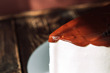 Piece of cake in white cream and brown glaze on wooden table