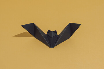 Origami bat made of black paper, isolated on gold or ocher background. Do it yourself decoration...