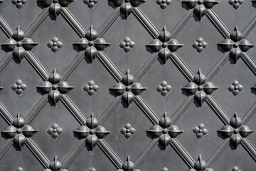 An antique black metal door with a forged pattern. Repetitive pattern of lines and geometric figures. Horizontal.