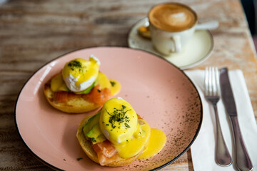 tasty poached eggs and smoked salmon toasts on pink plate with cup of cappuccino. Breakfast time