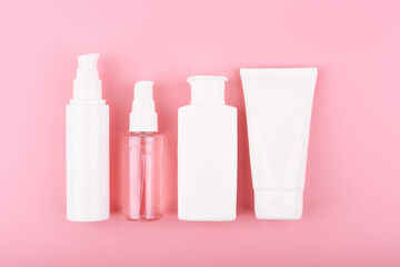 Trendy modern minimal flat lay with a set of beauty products in white tubes in a row against pink background. Concept of daily skin care routine 