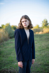 White man with long hair in dark clothes with forest behind