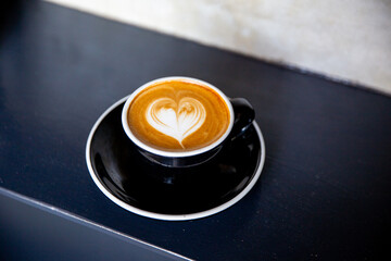 Black cup of cappuccino with latte art of heart shape on saucer on concrete background.