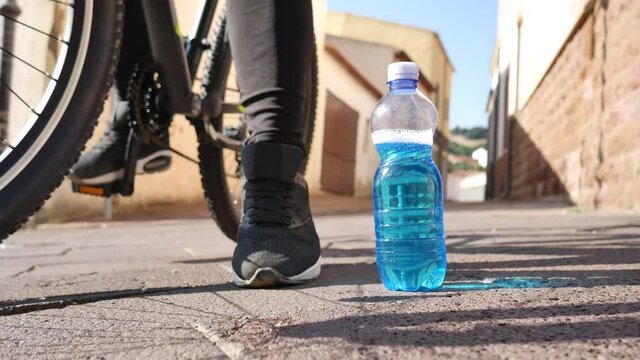 hand of a sporty girl on a MTB bicycle that collects the sports bottle from the ground with vitamins and supplements of blue color