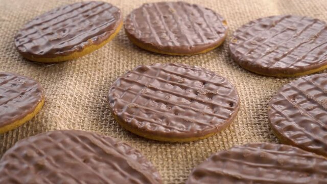 Digestive biscuits coated with dark chocolate on a rough rural sackcloth. Rotation. 4K video