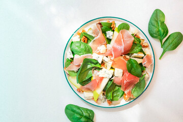 Pear salad with prosciutto, blue cheese, spinach, walnuts on white background, top view, copy space