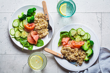 Quinoa, salted salmon, cucumber and broccoli on white plate, gray tile background. Healthy food concept.