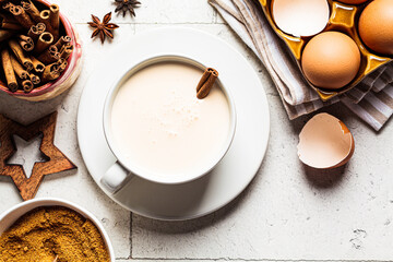 Christmas eggnog in white cup and ingredients on gray tile background, top view.