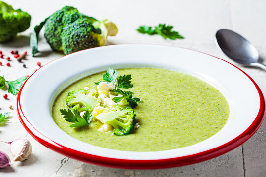 Broccoli soup puree with feta cheese in plate on gray tile background with ingredients.