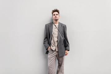 Fototapeta premium Stylish handsome young guy in fashionable clothes with a jacket and shirt with a purse on a gray background