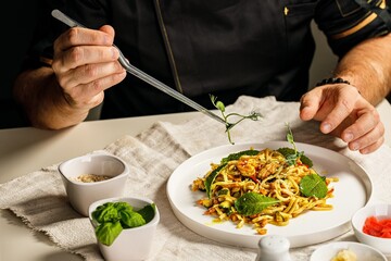 Spaghetti with seafood. The hands of the chef prepares a traditional pasta with seafood. The chef decorates the dish with herbs using tweezers. Restaurant serving dish. People work. Catering business