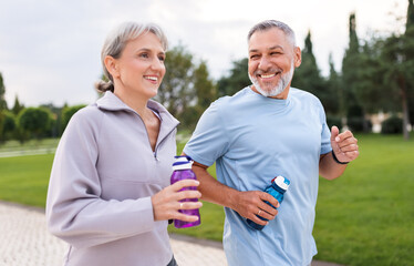 Lovely joyful retirees couple jogging outside in city park