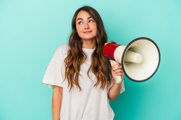 Young caucasian woman holding a megaphone isolated on blue background dreaming of achieving goals and purposes