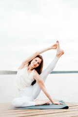 Portrait of beautiful Caucasian woman practising yoga on a lake shore. Flexibility, fit body.