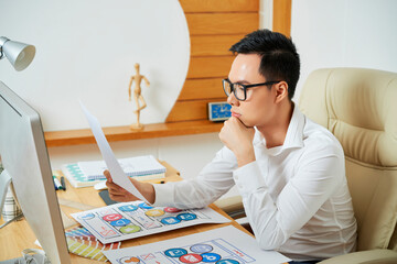 Pensive young UX designer reading document with requirement specification for new project